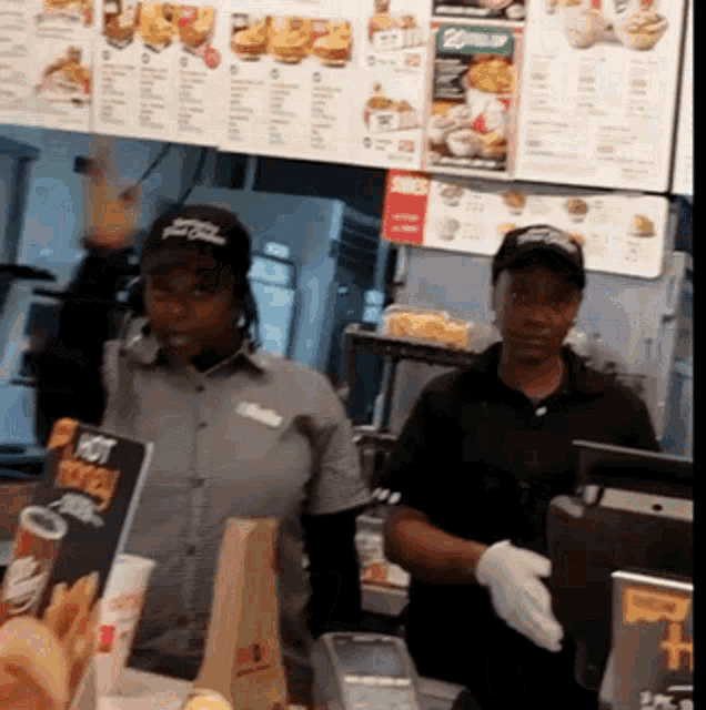 two mcdonald 's workers behind a counter with a sign that says hot chicken on it
