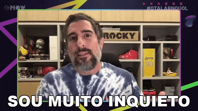 a man with a beard wearing a tie dye shirt says sou muito inqueto
