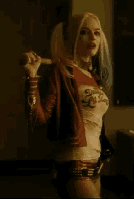a woman in a harley quinn costume is holding a bat and a microphone .