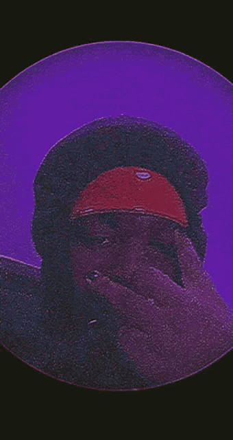 a person wearing a red hat covering their face in front of a purple background