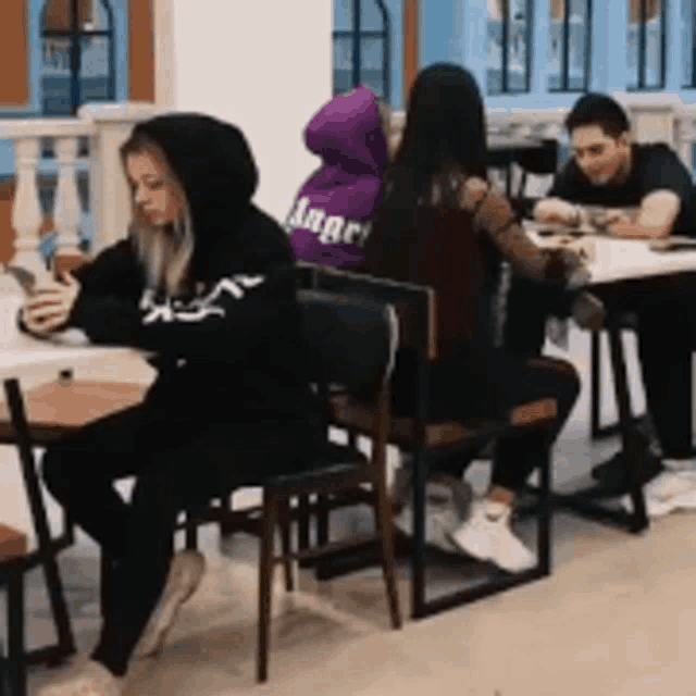 a group of people are sitting at tables with one woman wearing a purple angel hoodie