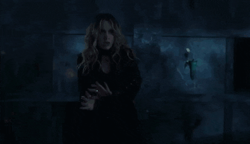 a woman in a black dress is standing in a dark room with green lights behind her .