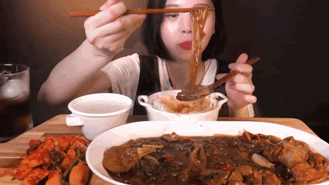 a woman is eating noodles with chopsticks and a bowl of soup