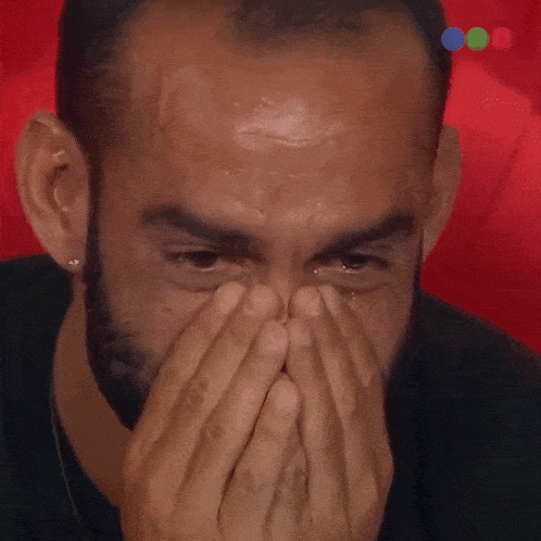 a man with a beard is covering his face with his hands and crying