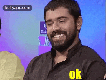 a man with a beard is wearing a black shirt with the word ok on the sleeve .