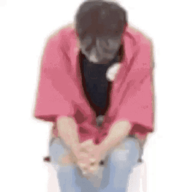 a man in a pink kimono is sitting on a chair with his hands folded in front of his face .