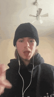 a young man wearing headphones and a beanie is giving a thumbs up