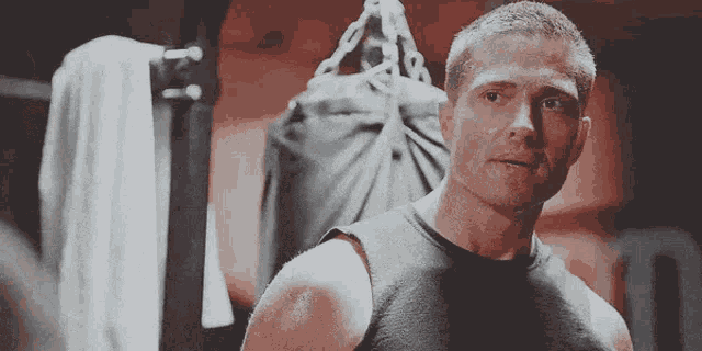 a man in a black tank top is standing in front of a punching bag .
