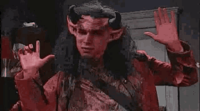 a man dressed as a devil with horns and ears is waving his hands in a dark room .