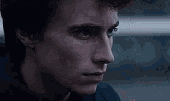 a close up of a young man 's face with a hand behind his back .
