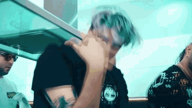 a man with purple hair is covering his face with his hand