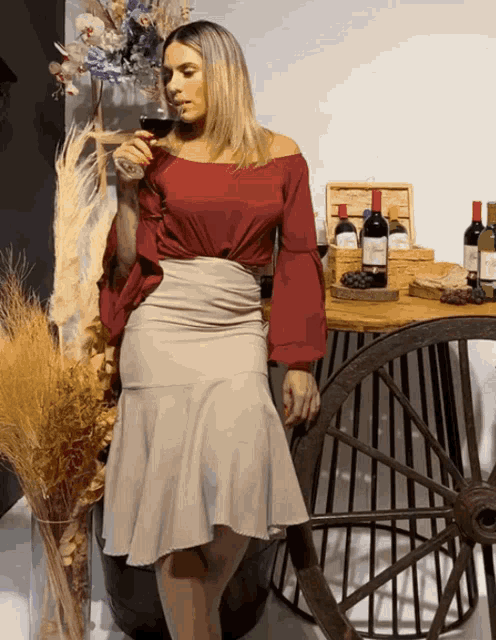a woman in a red off the shoulder top drinks wine