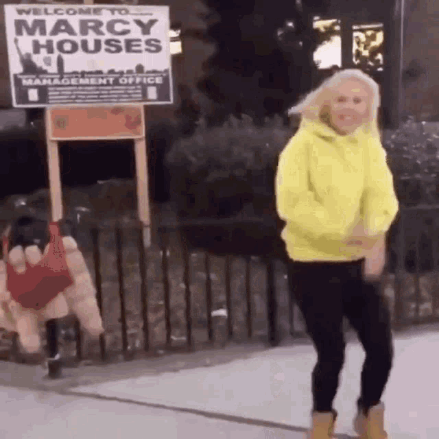a woman in a yellow hoodie is dancing in front of a sign that says marcy houses