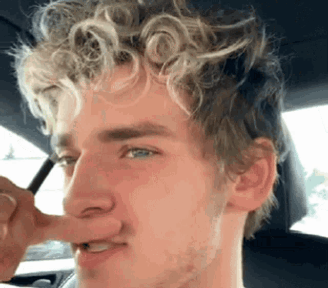 a young man with curly hair holds his nose in his hand