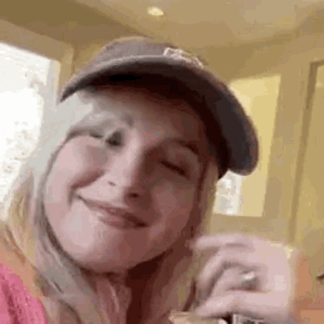 a woman wearing a baseball cap and a ring is smiling while holding a drink .