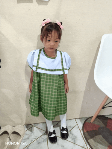 a little girl in a green and white dress is standing in front of a honor x6b