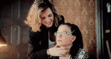 a woman is holding another woman 's neck while they are sitting next to each other in a room .