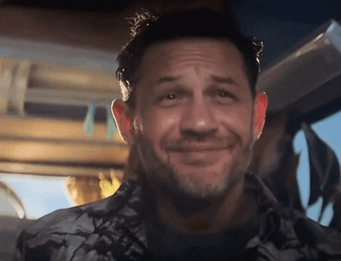 a man with a beard is smiling and looking at the camera while sitting in a car .
