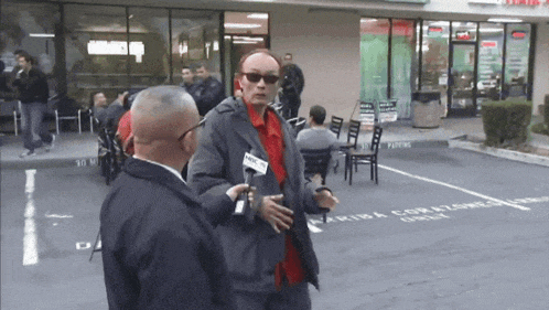 a man in a red shirt is being interviewed by a man in a gray jacket with a news channel sticker on his jacket