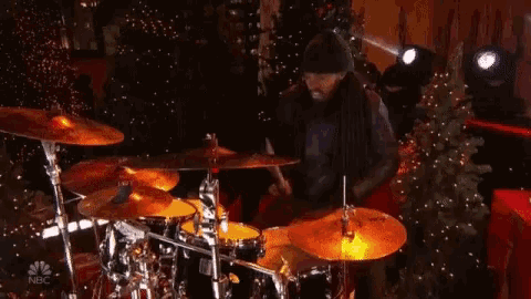 a man playing drums in front of a christmas tree with nbc written on the bottom