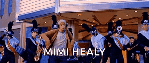 a man is dancing in front of a marching band with the words mimi healy on the bottom .