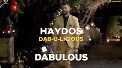 a man in a yellow suit is walking down a street with the words haydos dab-u-licious dabulous on the bottom .