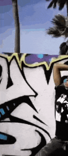 a person is standing in front of a wall with graffiti on it and a palm tree in the background ..