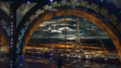 a man in a suit stands in front of a painting of the eiffel tower at night