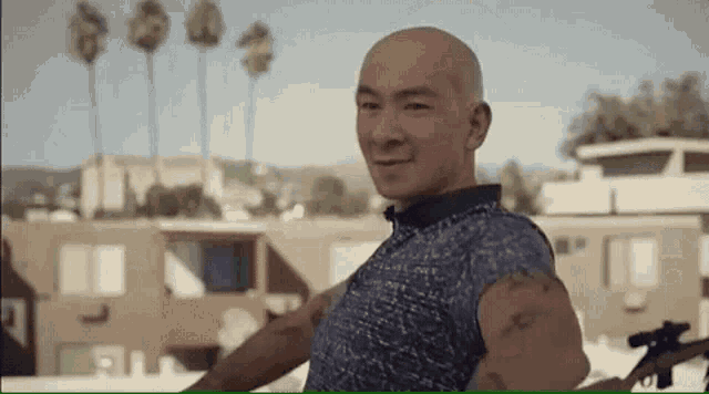 a bald man with a tattoo on his arm is standing in front of a building and smiling .