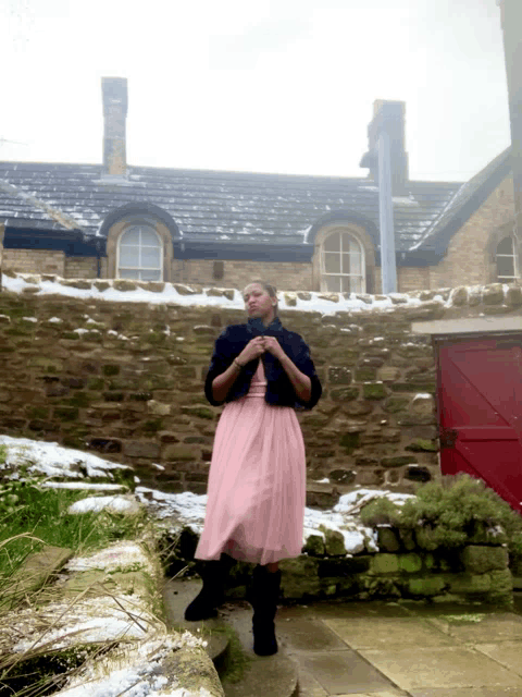 a woman in a pink dress is standing in front of a house
