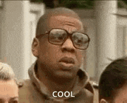 a man wearing glasses is standing in a crowd of people and says `` cool '' .