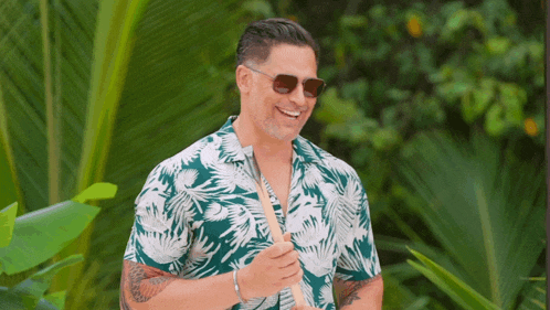 a man wearing a hawaiian shirt and sunglasses smiles