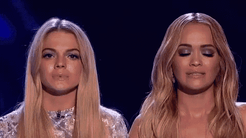 two women are standing next to each other on a stage with their faces covered .