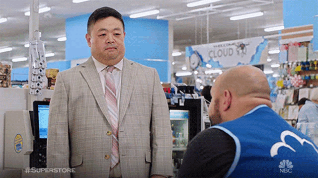 a man in a suit and tie is talking to a man in a blue vest with the word superstore on it