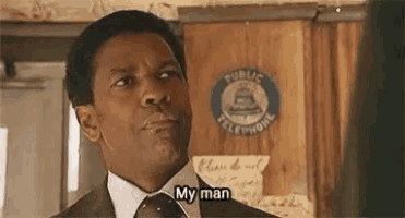 a man in a suit and tie is standing in front of a wooden sign that says `` my man '' .