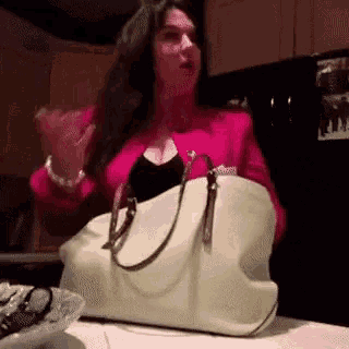 a woman in a pink jacket is holding a white purse in her hands .