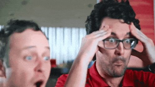 a man with glasses and a red shirt holds his head