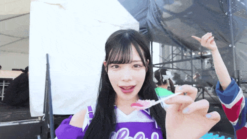 a girl in a purple shirt is holding a spoon with a pink candy on it