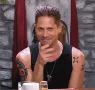 a man with tattoos on his arms is sitting at a table with his hand on his chin