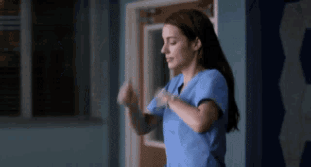 a nurse in a blue scrub top is dancing in a room .