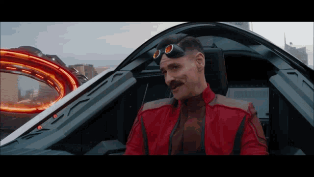 a man in a red jacket and goggles is sitting in a futuristic vehicle
