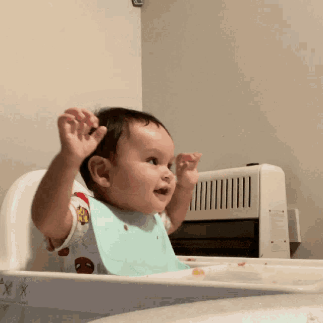 a baby wearing a bib is sitting in a high chair with his arms in the air