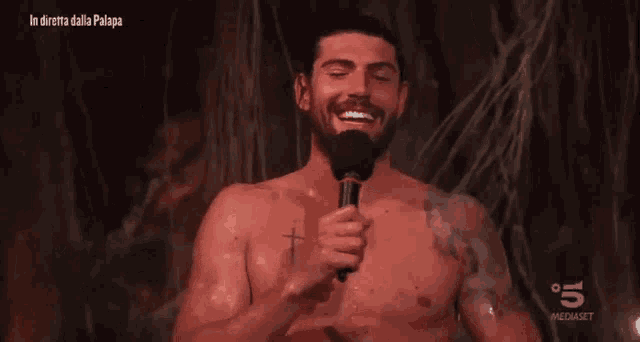 a shirtless man is holding a microphone in front of a screen that says " in diretta dalla palapa "