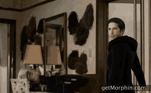 a man in a black hoodie stands in front of a wall of wigs with the website getmorphin.com below him