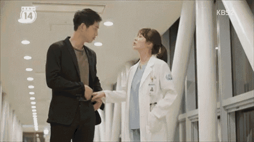 a man and a woman are standing next to each other in a hallway holding hands .