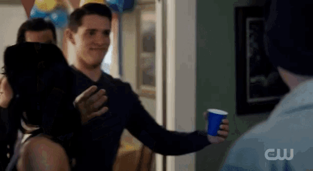 a man holding a blue cup with the cw logo on the bottom