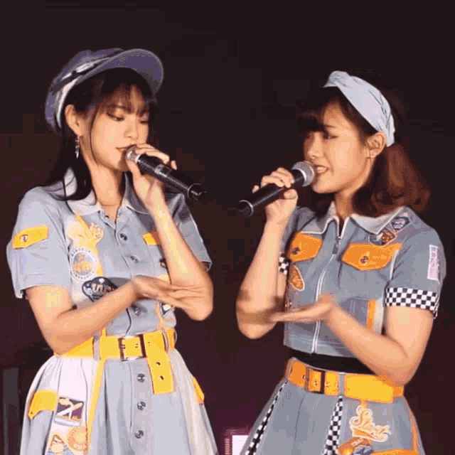two girls singing into microphones with one wearing a shirt that says ' sns ' on it
