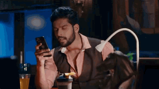 a man with a beard is sitting at a table looking at his phone .