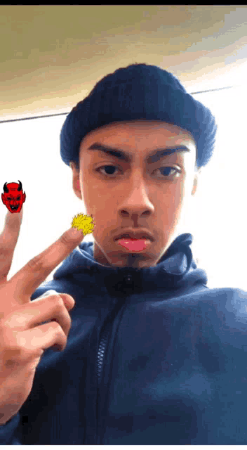 a young man wearing a black beanie and a blue jacket has a devil on his finger