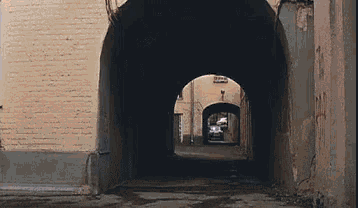 a dark tunnel between two buildings with a car driving through it